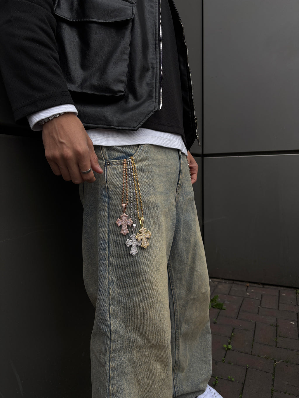 Person wearing a black jacket and green jeans with decorative elements, standing against a dark background.
