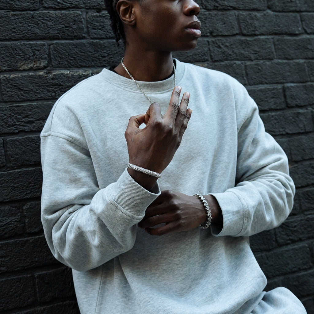 Person wearing a white sweatshirt and pants against a dark brick wall