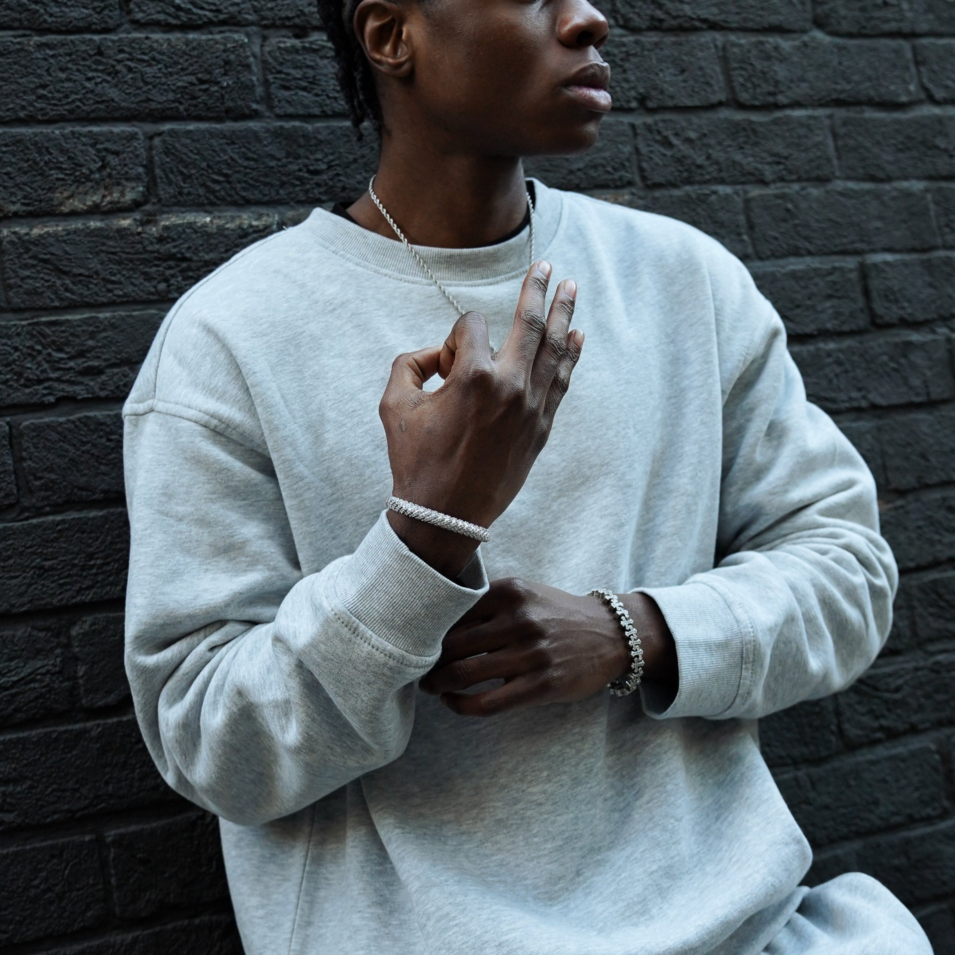 Person wearing a white sweatshirt and pants against a dark brick wall