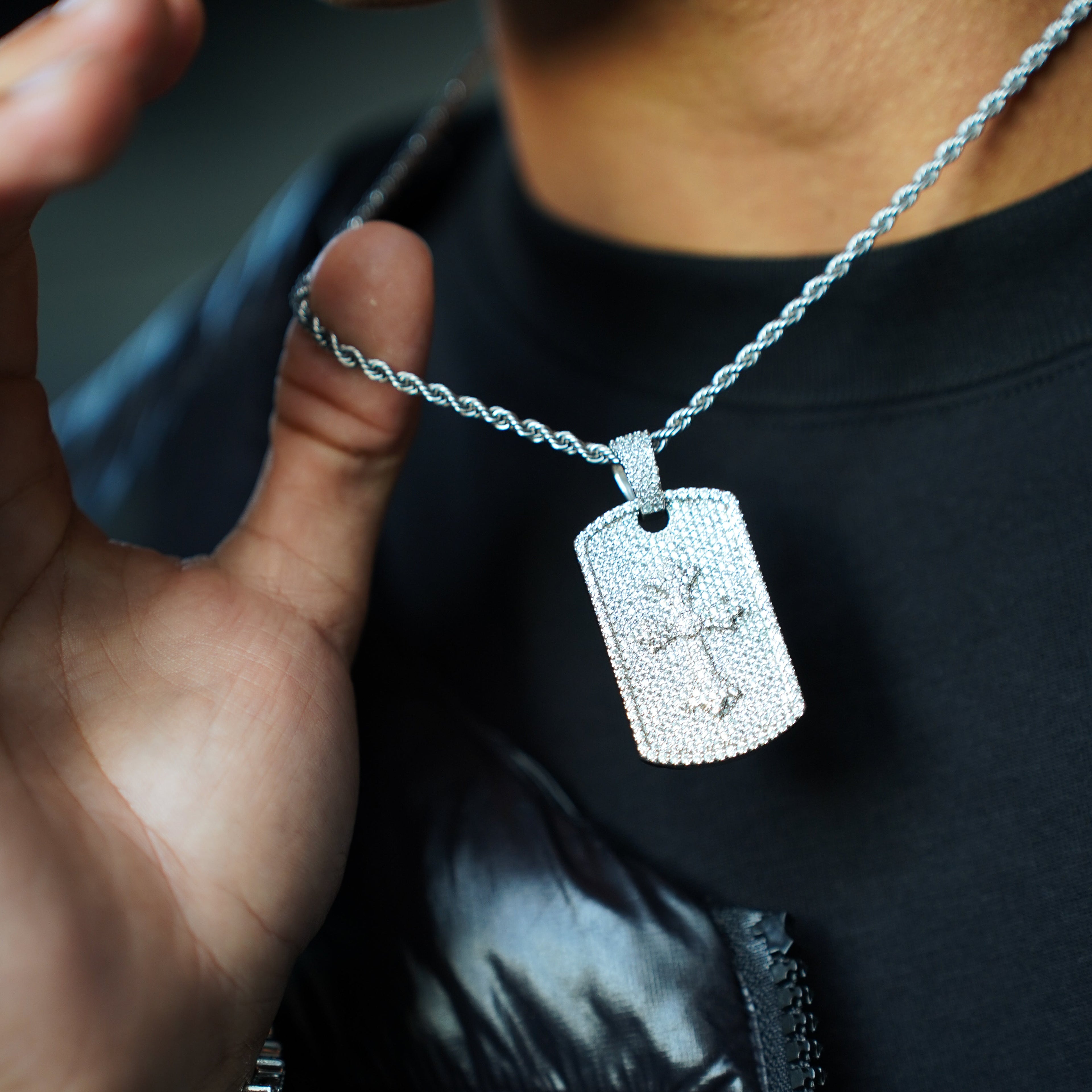 Person wearing a black jacket with a silver chain and dog tag necklace.