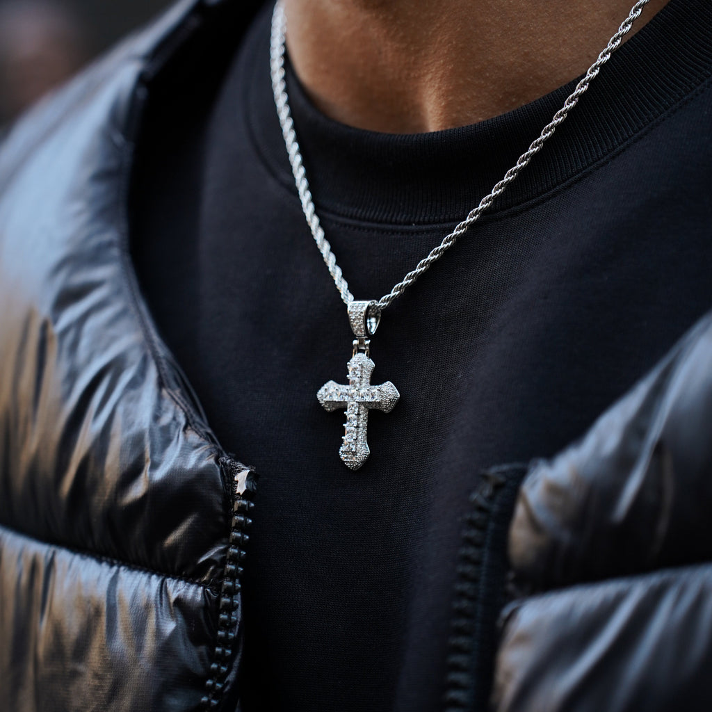 Person wearing a black jacket with a silver chain necklace featuring a cross pendant.