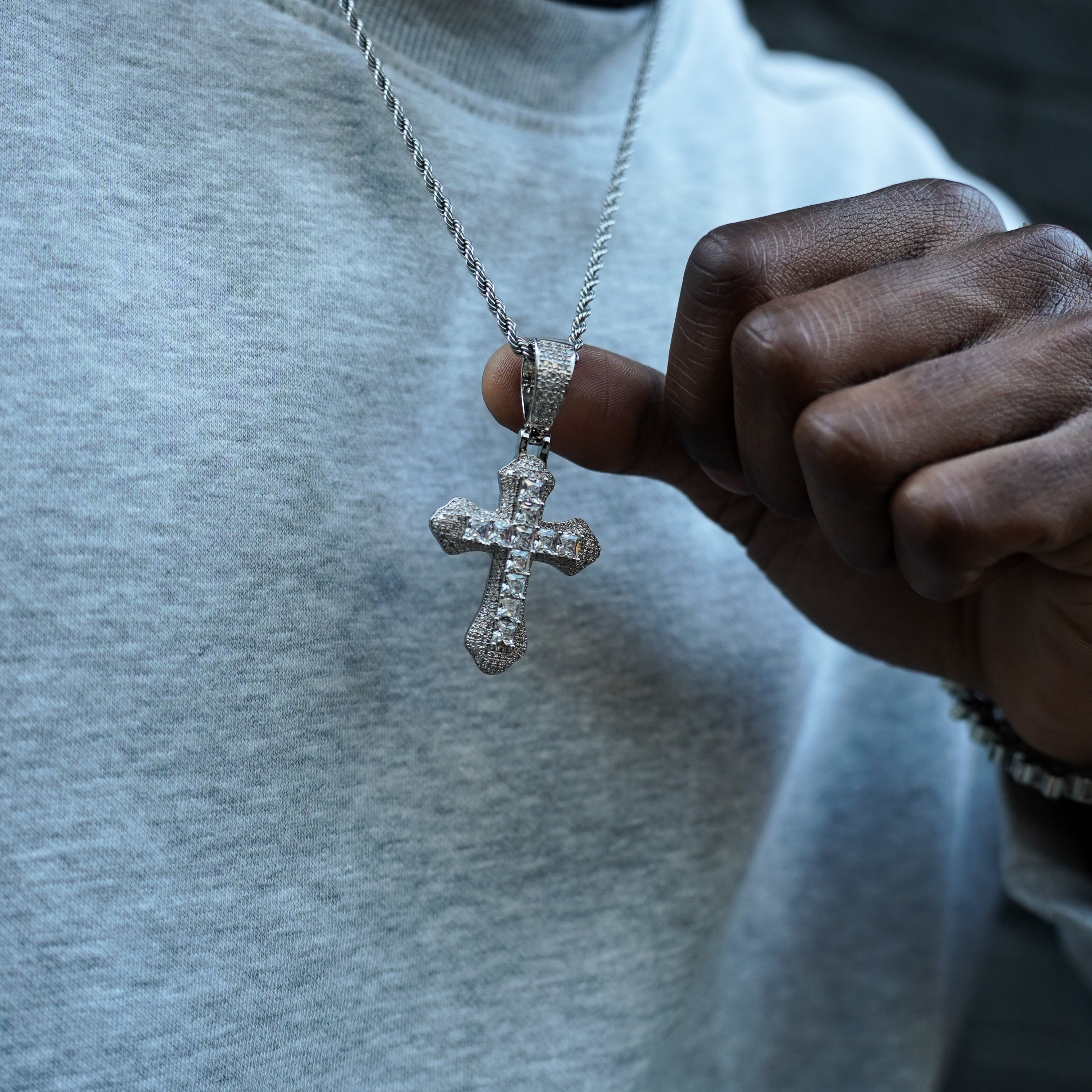 Person wearing a cross necklace and bracelet, with a blurred background