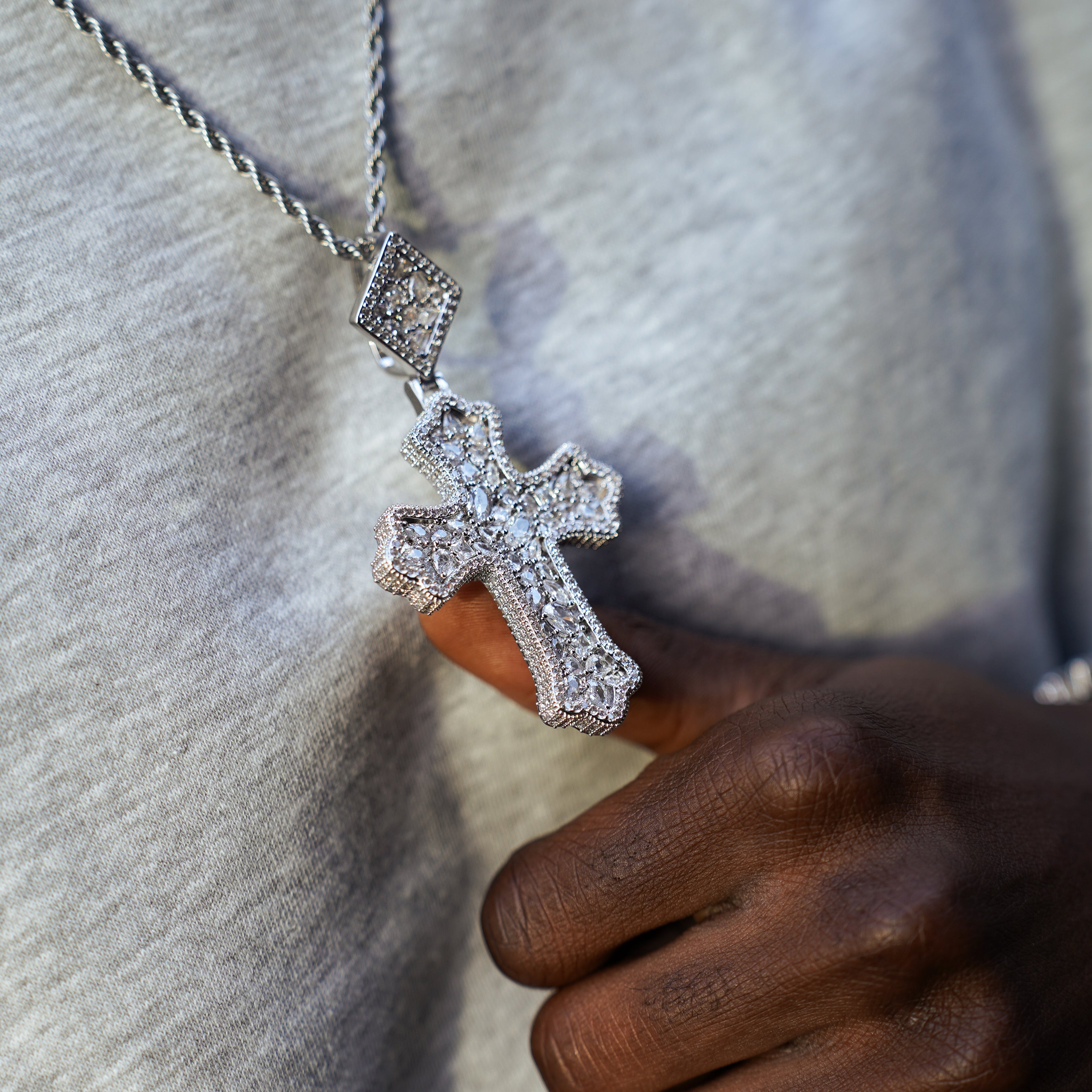 Close-up of a hand holding a silver cross pendant necklace against a neutral background