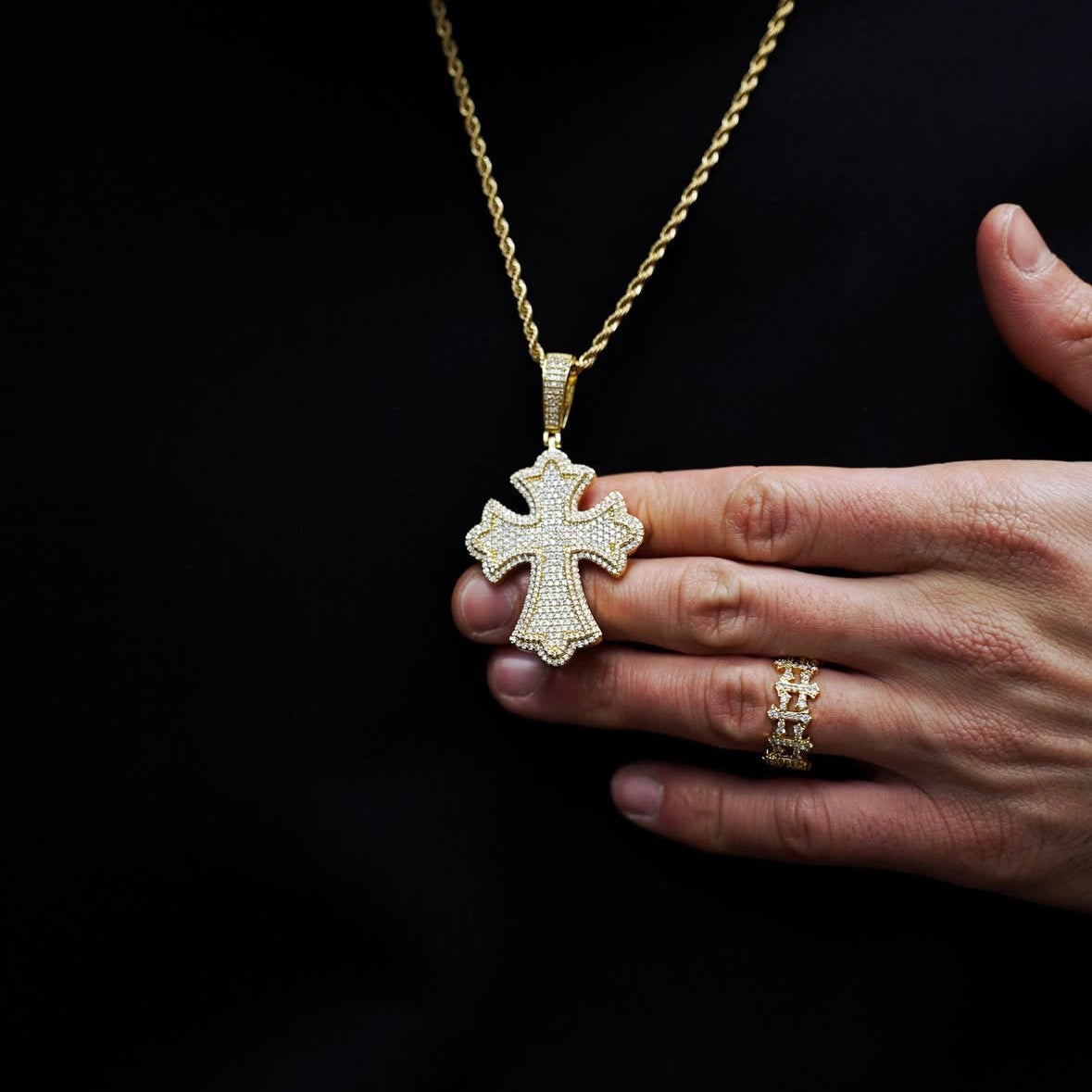 Gold cross pendant necklace held by a hand against a black background