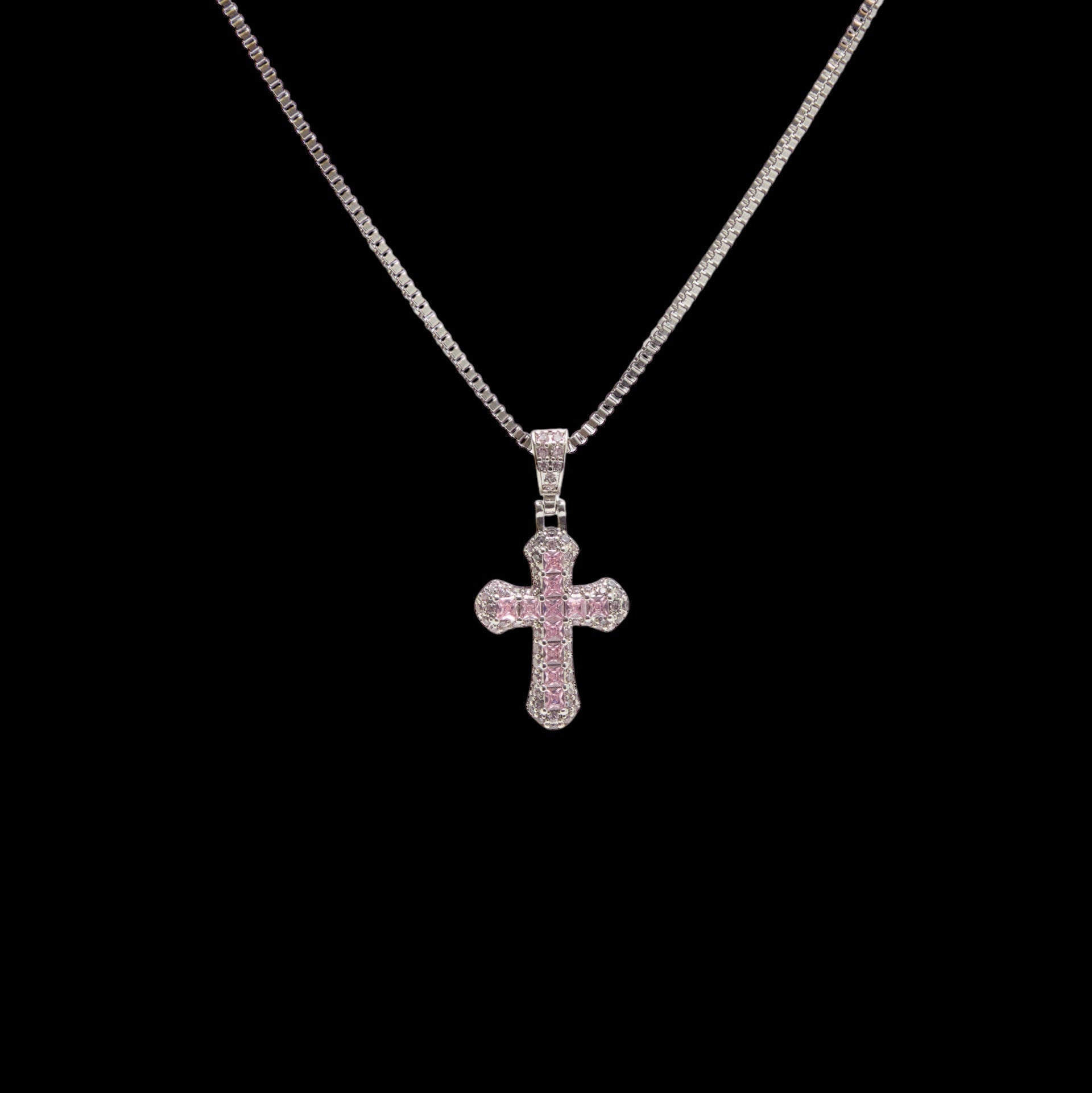 Cross-shaped pendant with pink stones on a chain against a black background